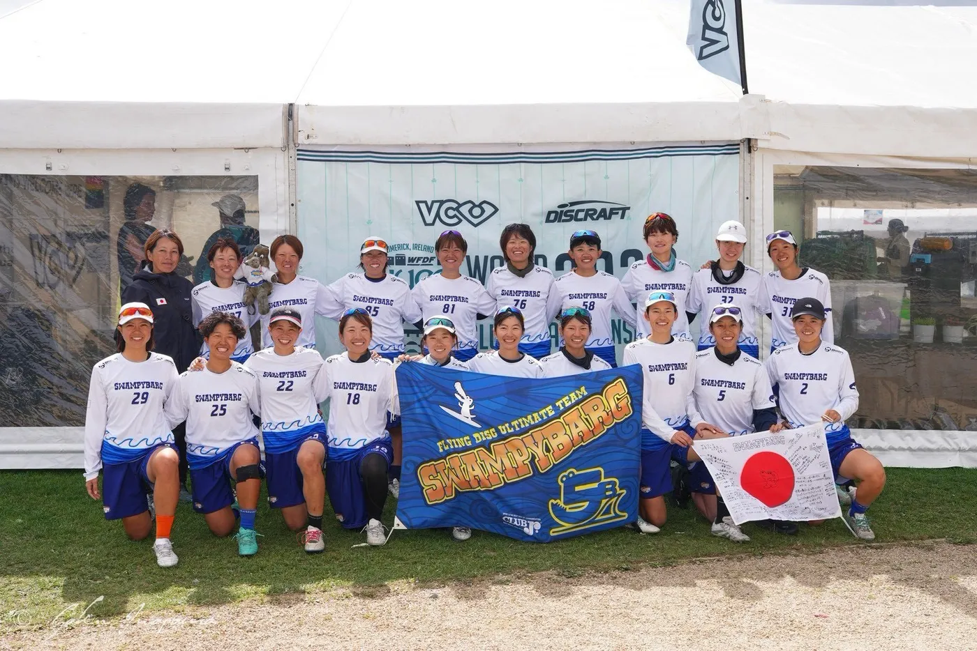 チームの横断幕と寄せ書きの日の丸を持つSWAMPYBARGの集合写真